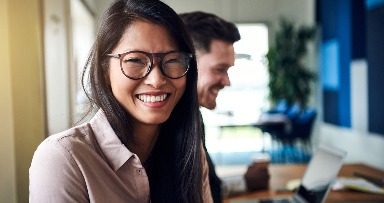 Smiling young Asian businesswoman sitting with colleagues in an office